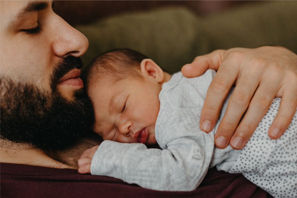 Neonato che dorme sereno sul petto del padre che lo guarda con amore